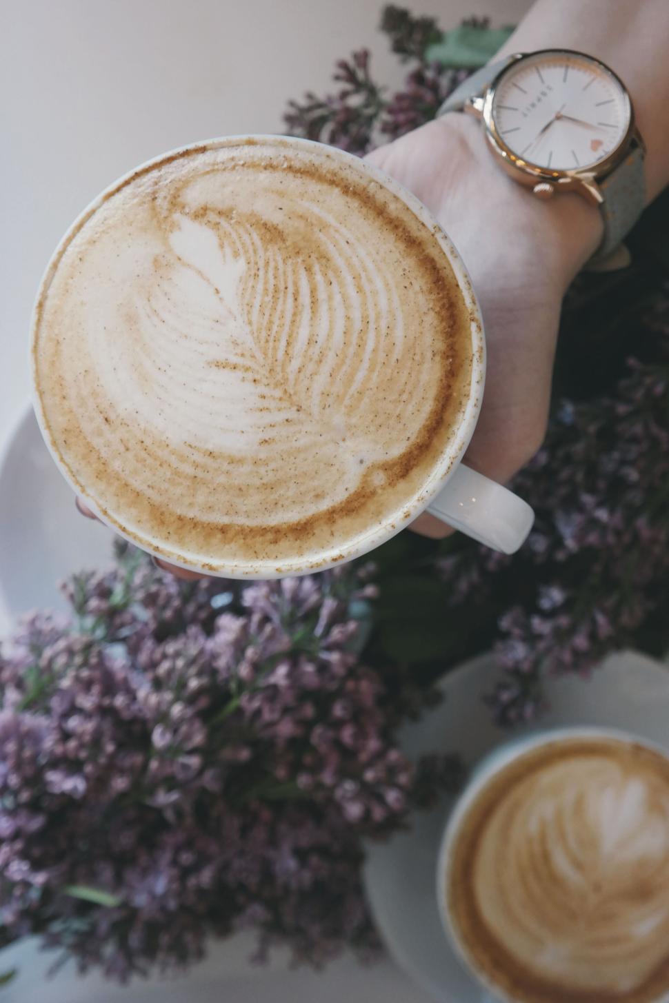 Free Image of Cup of latte art coffee surrounded by flowers. 