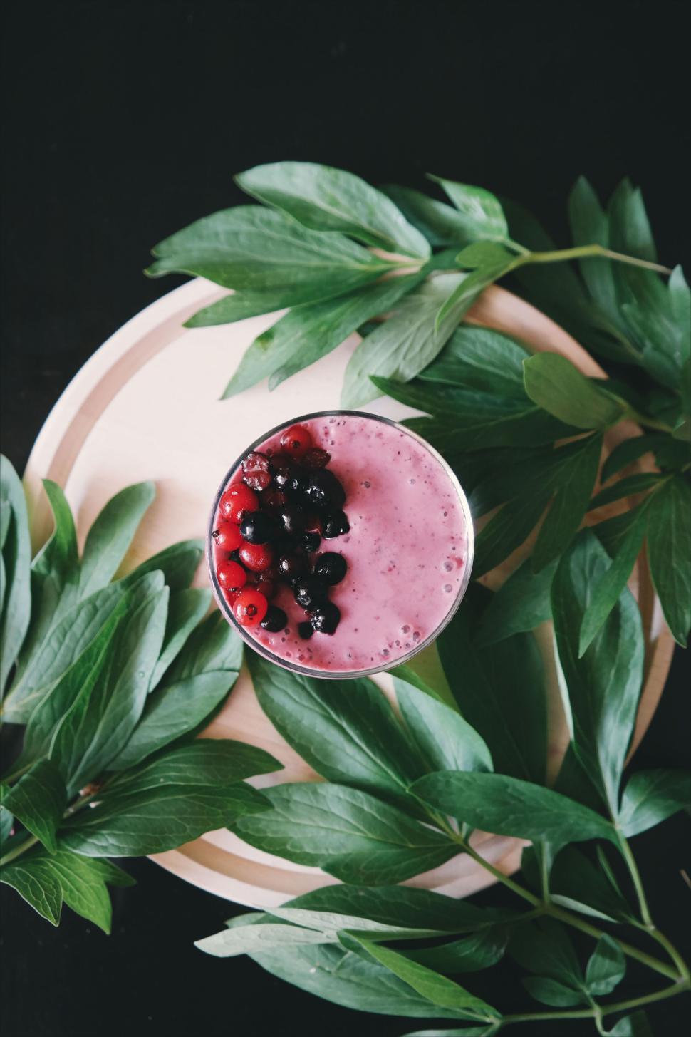 Free Image of Pink berry smoothie surrounded by green leaves 