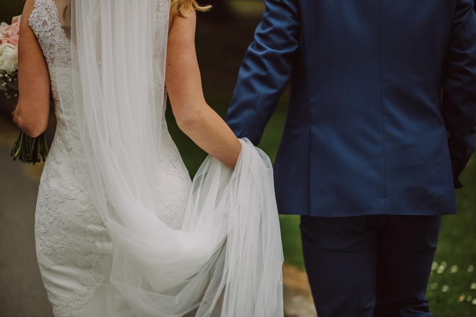 Free Image of Bride and groom holding hands walking together outdoors 