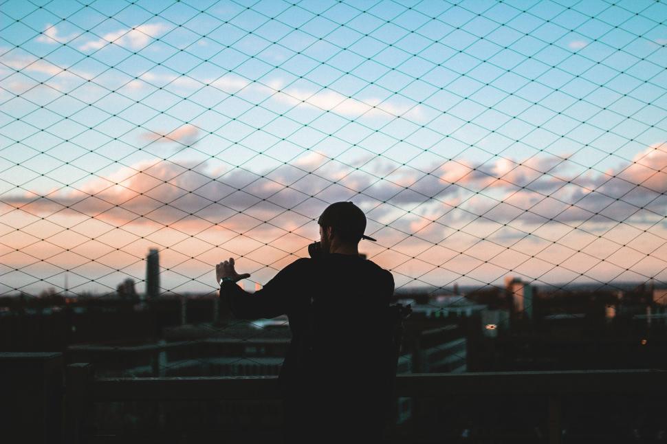 Free Image of Silhouette of person looking over city through fence net. 