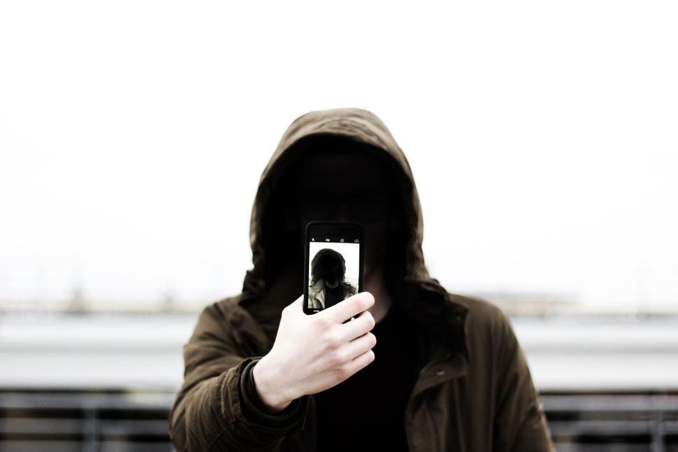 Free Image of Person holding phone in front of face wearing hood. 