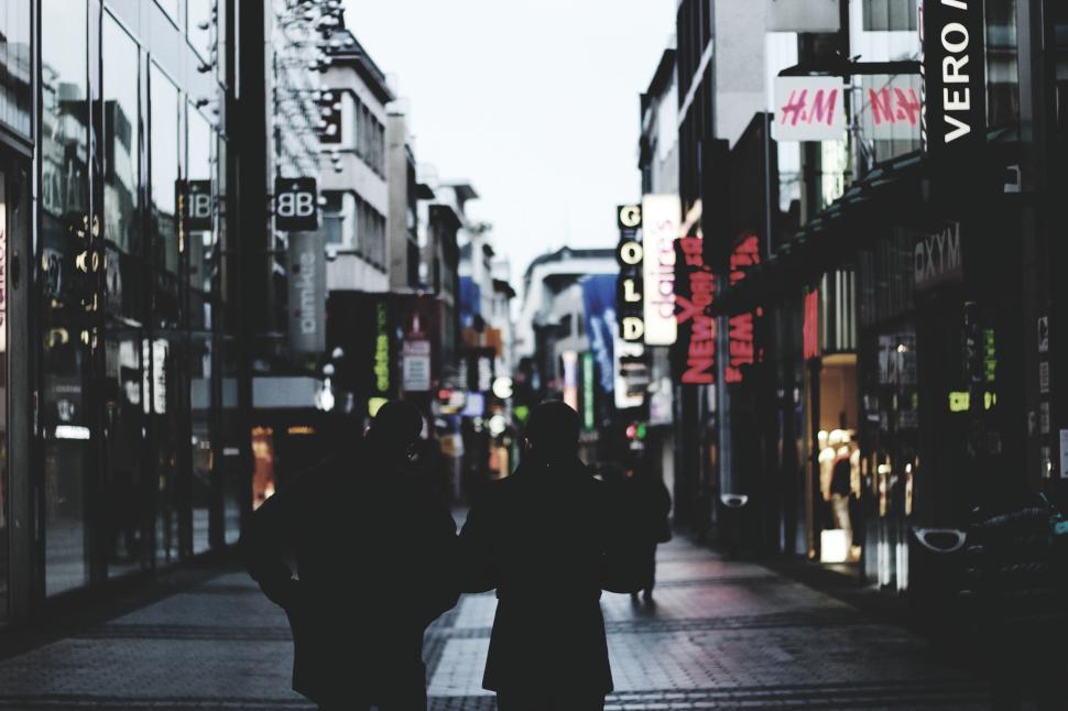 Free Image of Two people walking down a bright commercial street. 