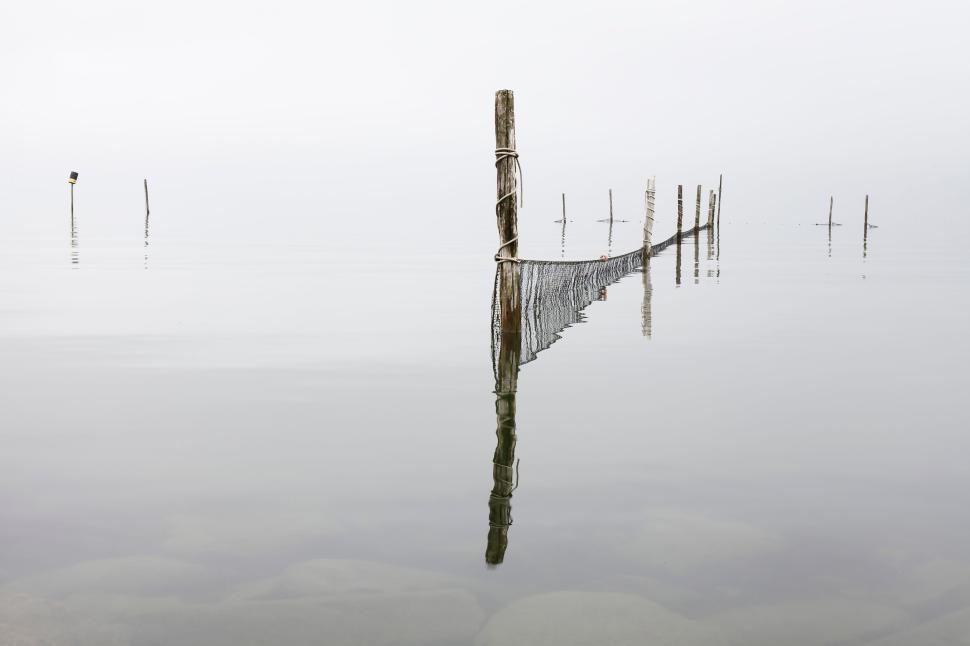 Free Image of Serene foggy lake with wooden posts and fishing net. 