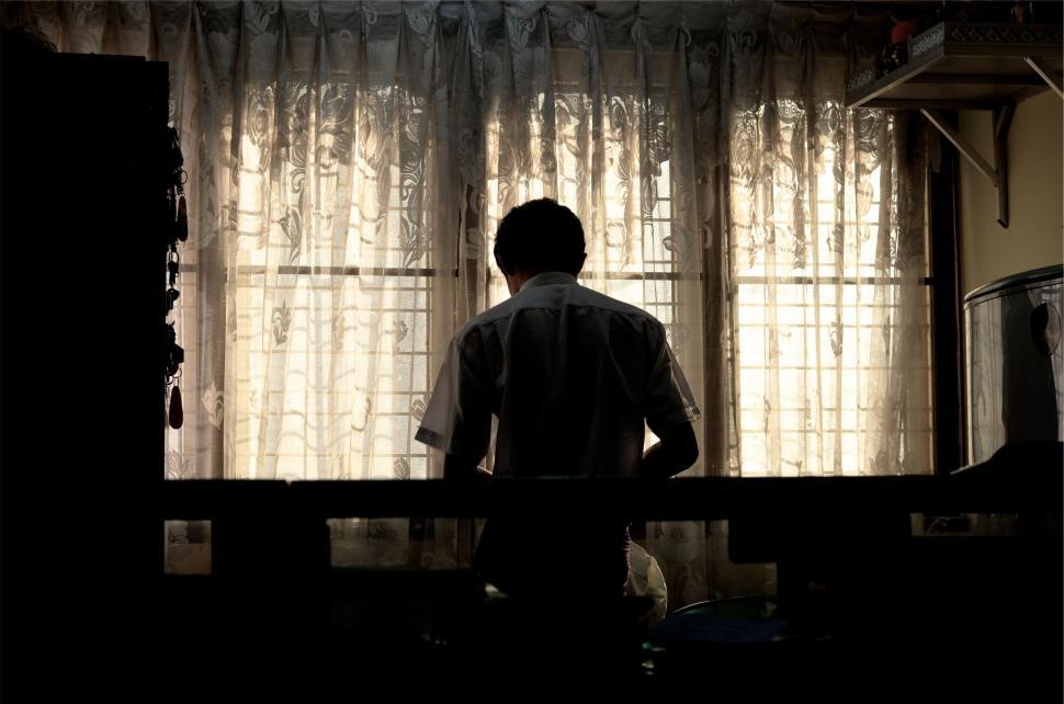 Free Image of Person silhouetted by window with light peeking through. 