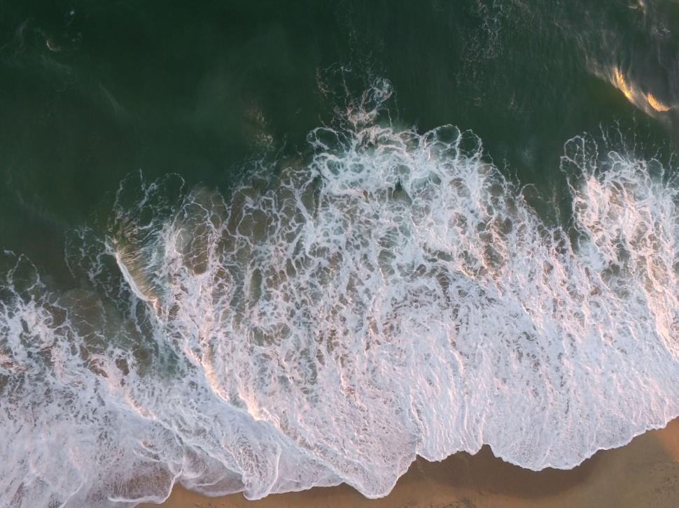 Free Image of Waves crashing on sandy shore viewed from above. 