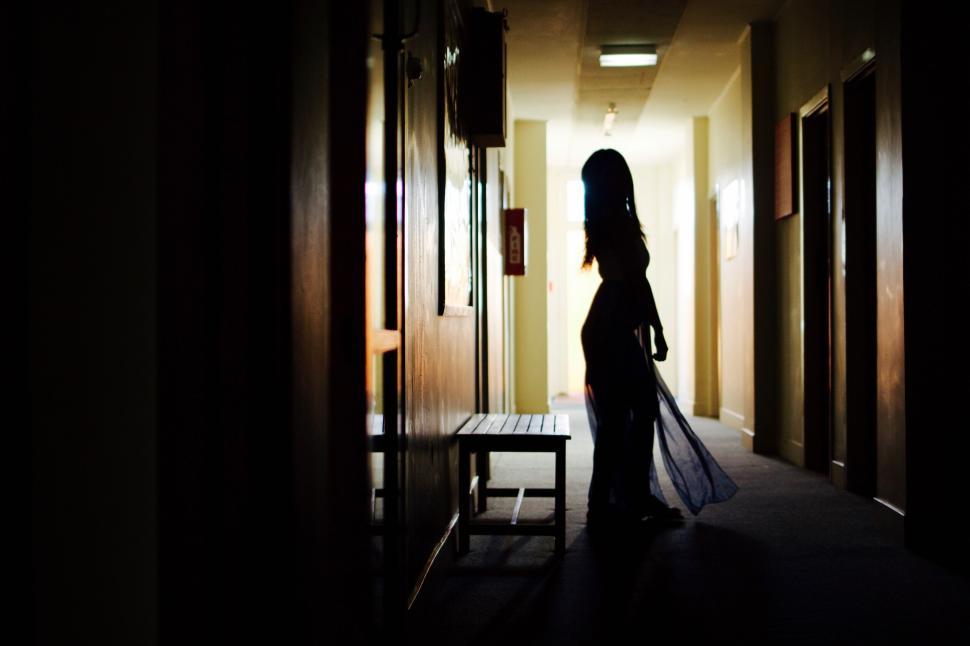 Free Image of Silhouetted woman standing alone in a dimly lit hall. 