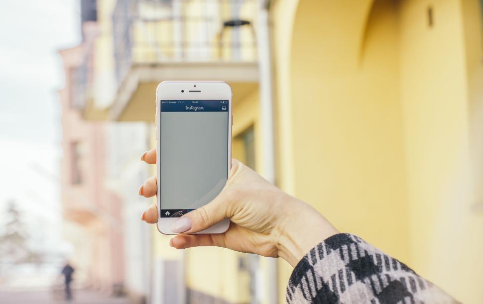 Free Image of Hand holding a smartphone in front of buildings 