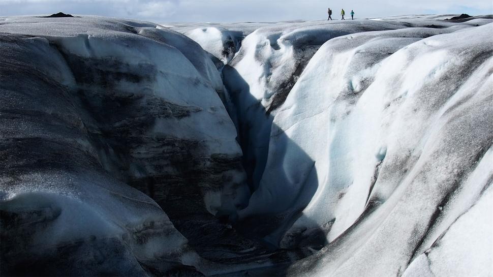 Free Image of Hikers walking across large glacier crack under sky 