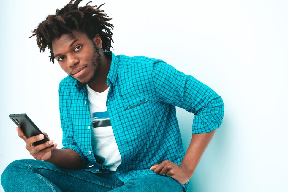 Free Image of Man sitting with smartphone in hand against blue background. 