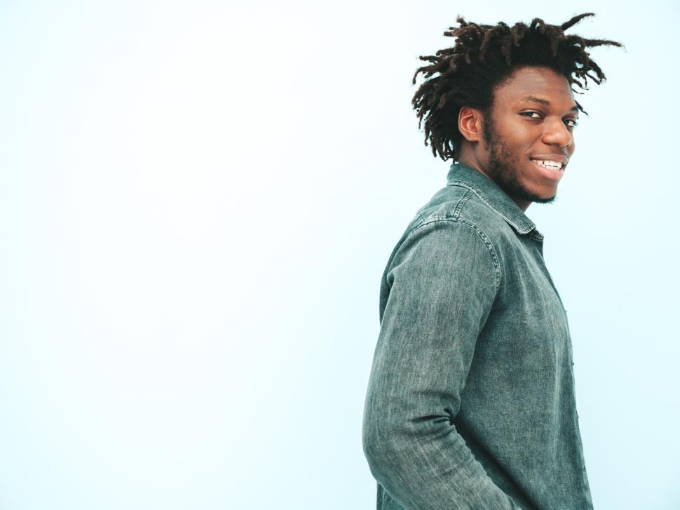 Free Image of Man in denim shirt smiling, standing against wall. 
