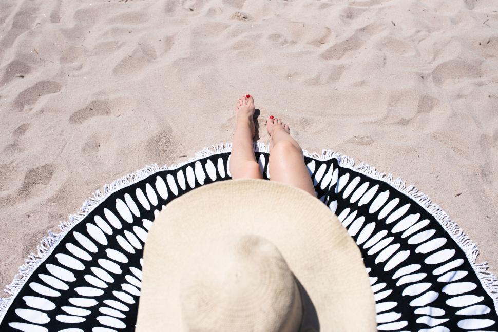 Free Image of Person Relaxing on Sandy Beach with Round Towel and Hat 