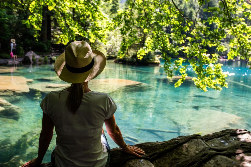 Free Image of Woman in hat by crystal clear blue lake on sunny day 