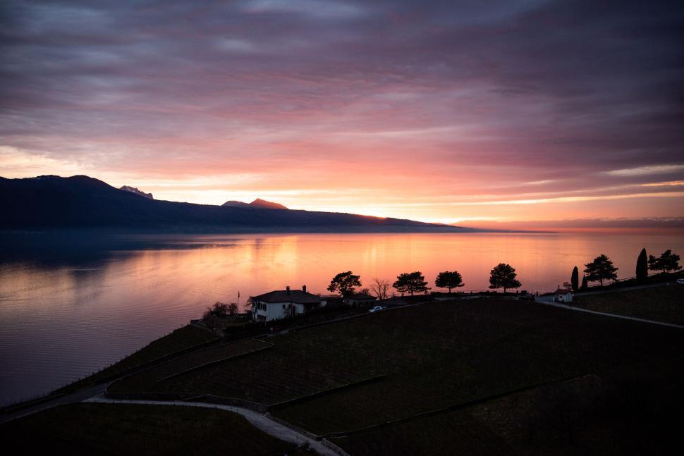 Free Image of Sunset over calm lake with silhouetted landscape 