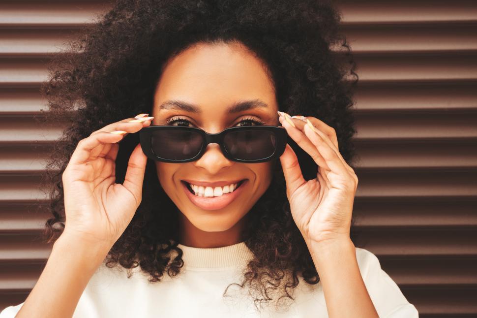 Free Image of Woman with curly hair smiling, wearing sunglasses close-up. 