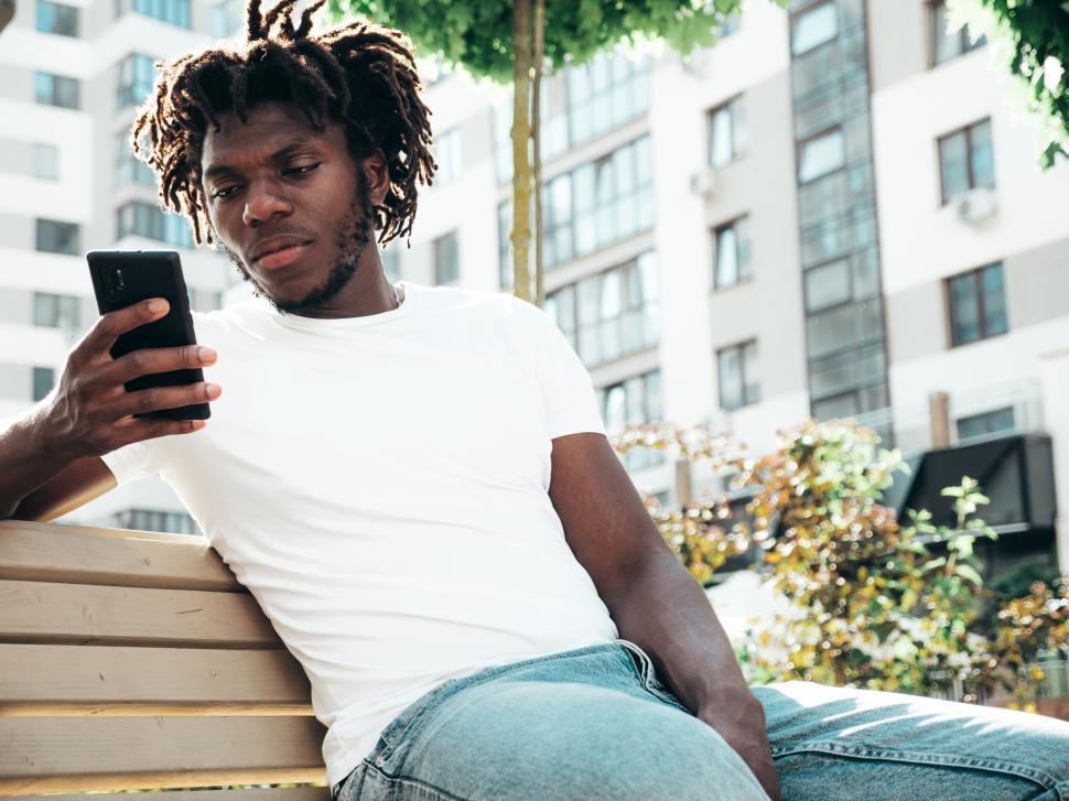 Free Image of Man sitting on bench with phone in an urban park setting 