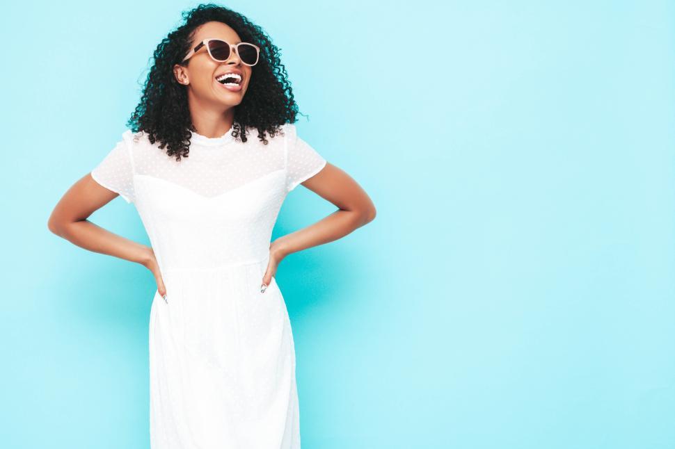 Free Image of Joyful woman in white dress with hands on hips, laughing 