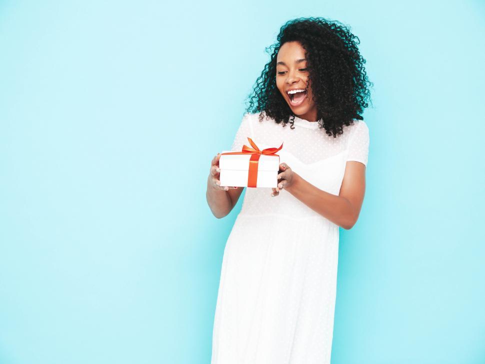 Free Image of Excited woman in white dress holding gift box with orange bow 