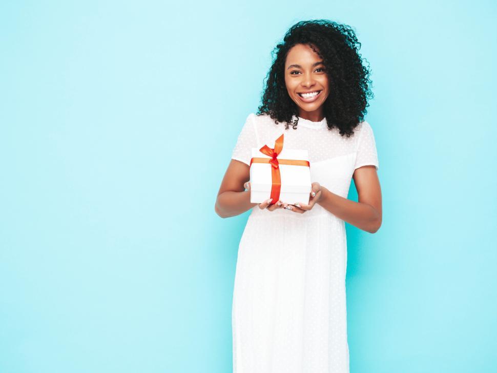 Free Image of Smiling woman in white dress presenting gift box with bow 