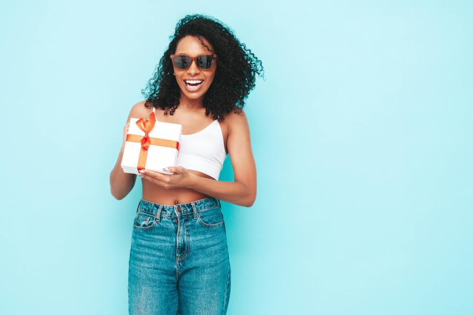 Free Image of Woman with gift box in jeans and top smiling happily 