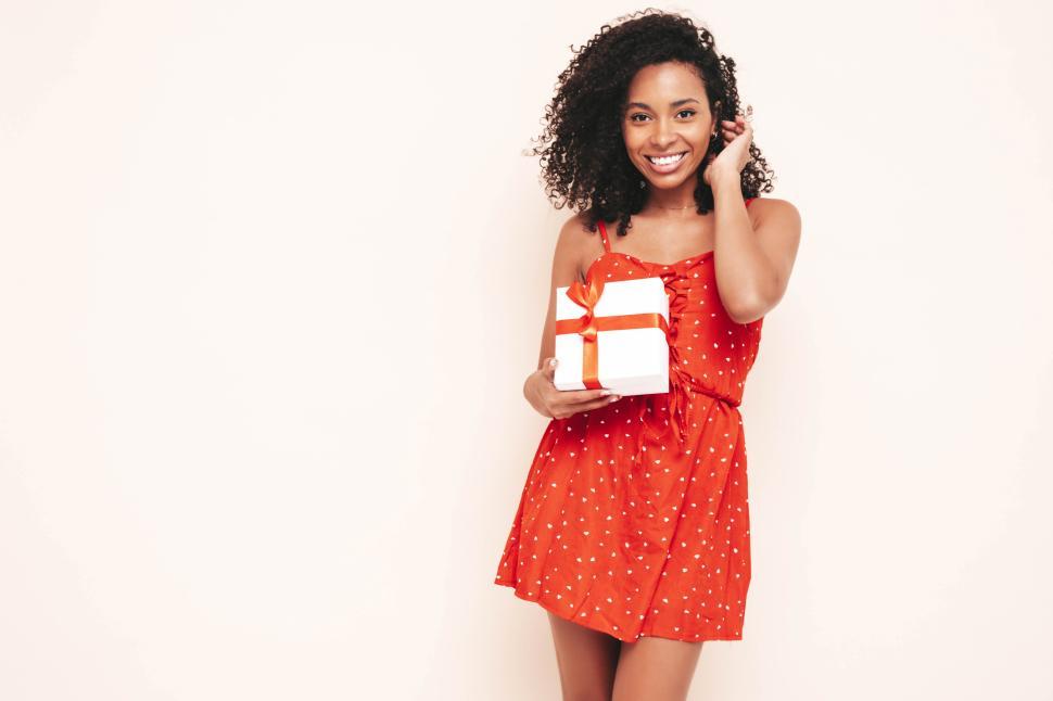 Free Image of Woman with gift box in red dress smiling radiantly 