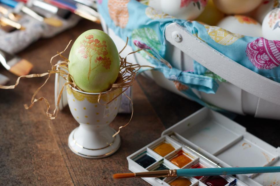 Free Image of Decorated pastel-colored egg in holder with paint nearby 