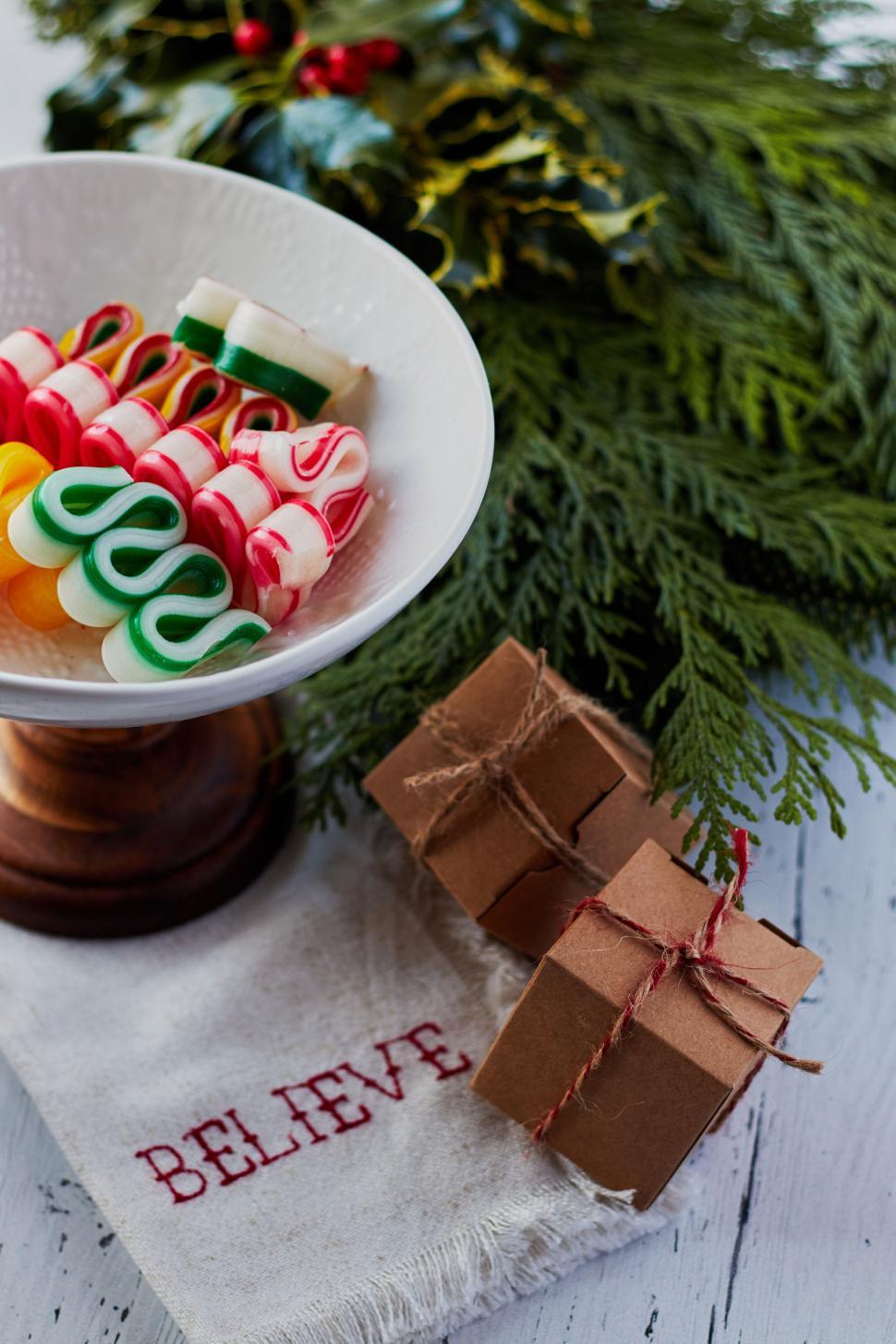 Free Image of Festive candies in bowl with gifts and green foliage. 
