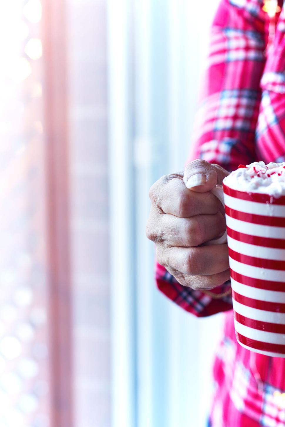 Free Image of Hand holding striped mug with whipped cream topping. 