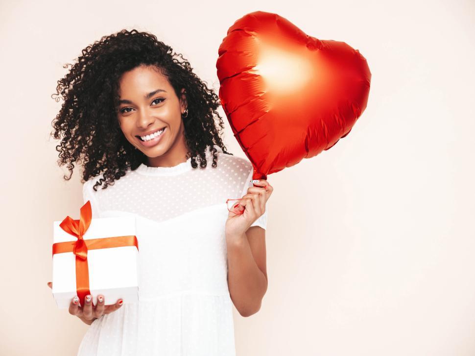 Free Image of Woman holding red heart balloon and gift box smiling. 