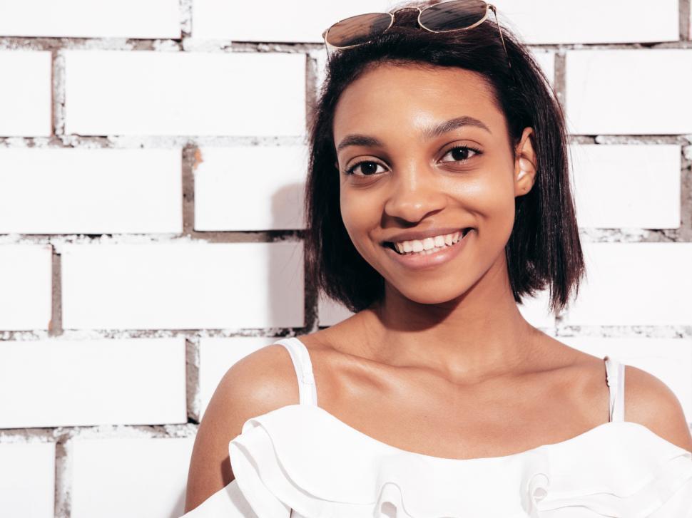 Free Image of Close-up of woman in white ruffled top by brick wall. 