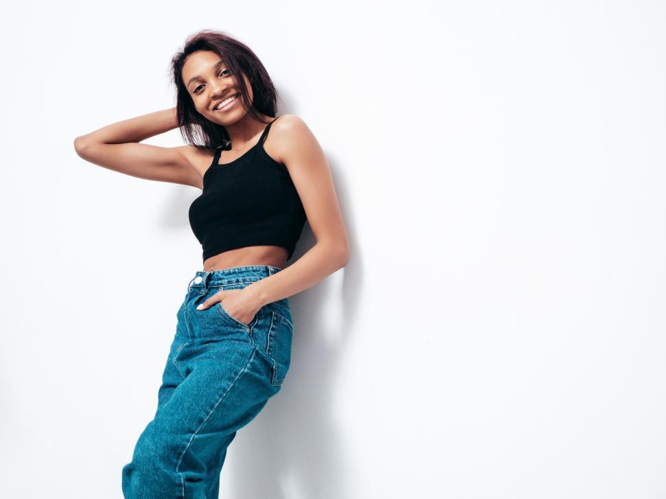 Free Image of Woman posing against white wall, black top, blue jeans 