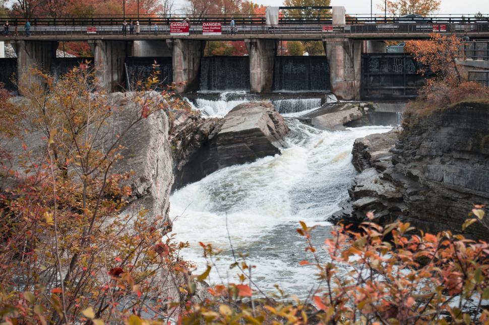 Free Image of Rushing water through a dam surrounded by autumn leaves 