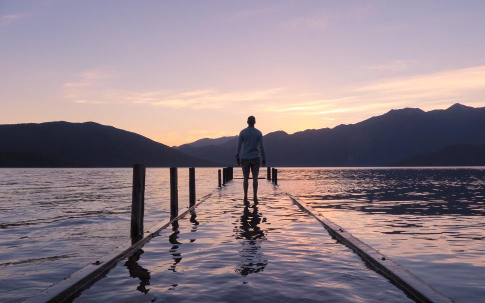 Free Image of Person standing on pier at sunrise over tranquil lake 