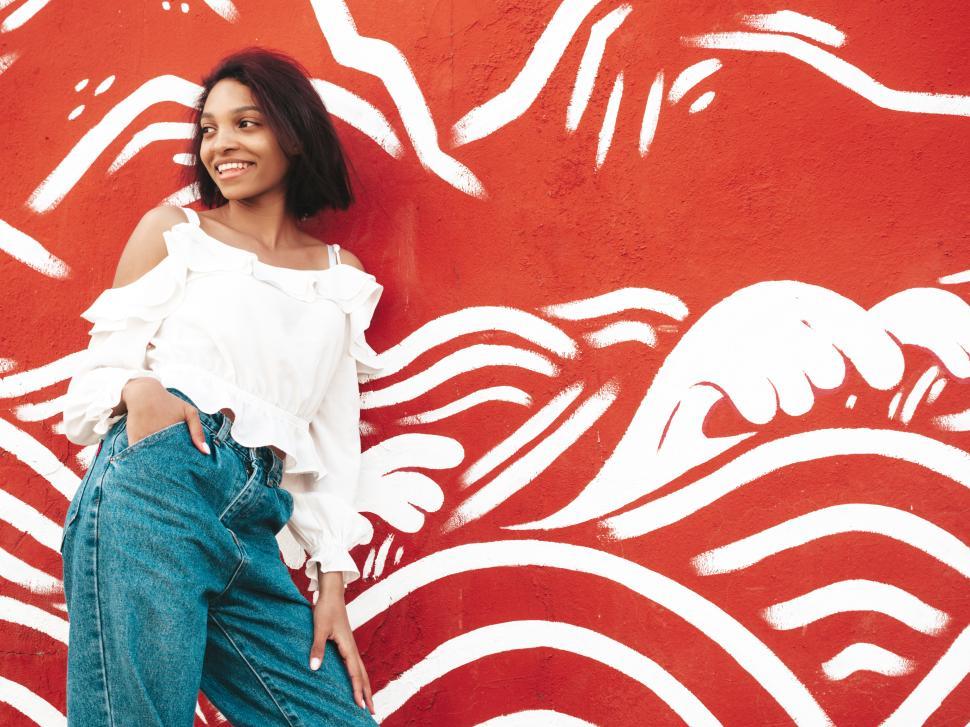 Free Image of Woman artistic pose, red wall white patterns, casual jeans 