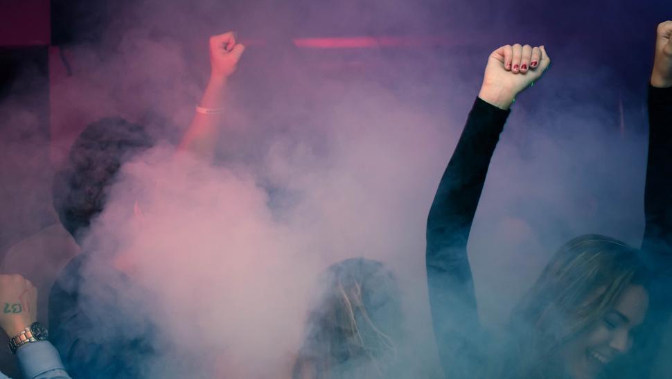 Free Image of Crowd raising arms in a smoky and vibrant party environment 