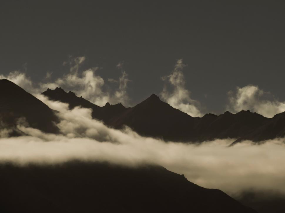 Free Image of Misty mountain range peaks with clouds beneath starry sky 