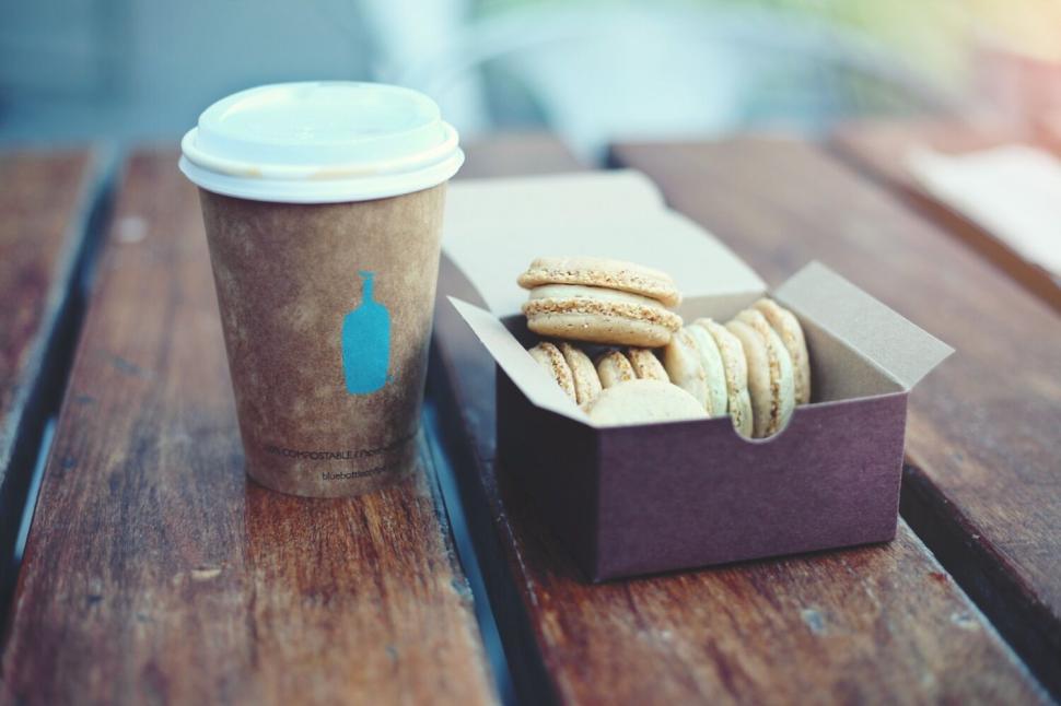 Free Image of Cup of coffee and box of macarons on wooden table outside 