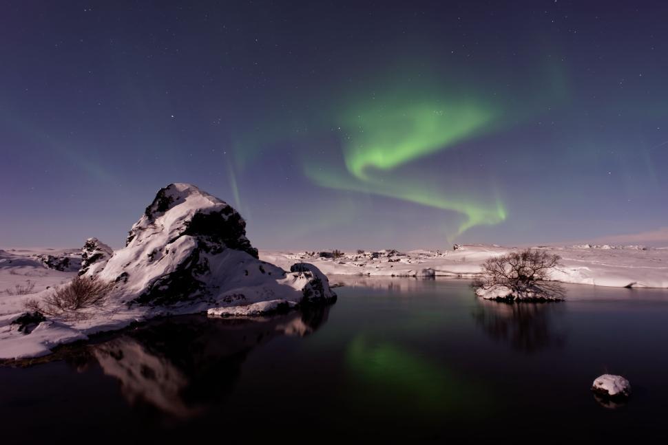 Free Image of Northern lights reflected in still water beneath rocks 
