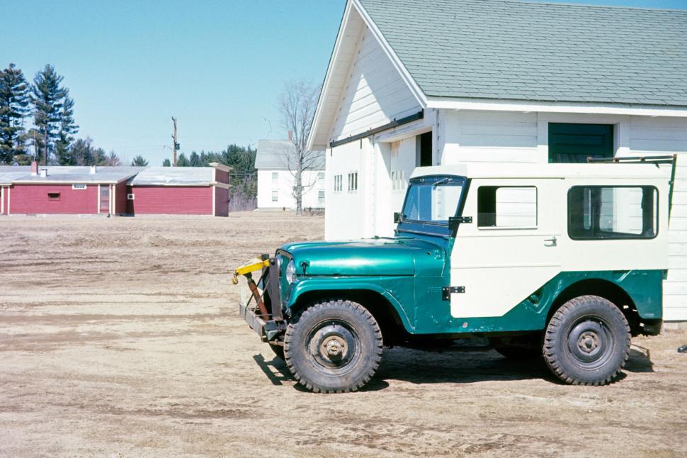 Free Image of Vintage jeep parked beside a white building on dirt 