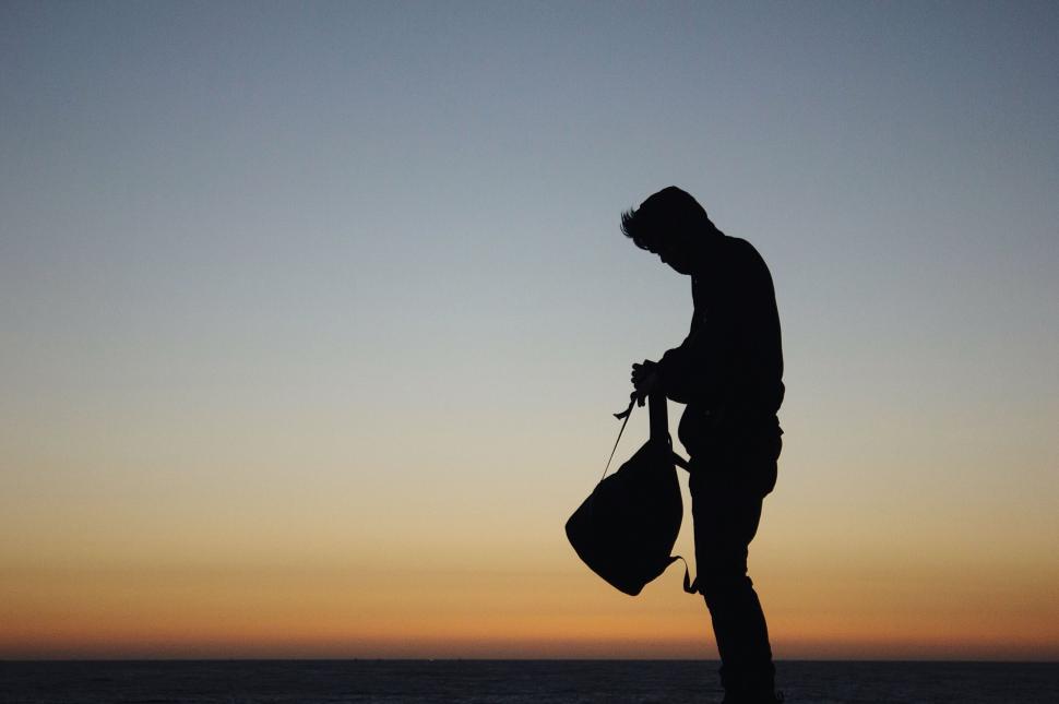 Free Image of Silhouette of a man standing with bag at sunset 