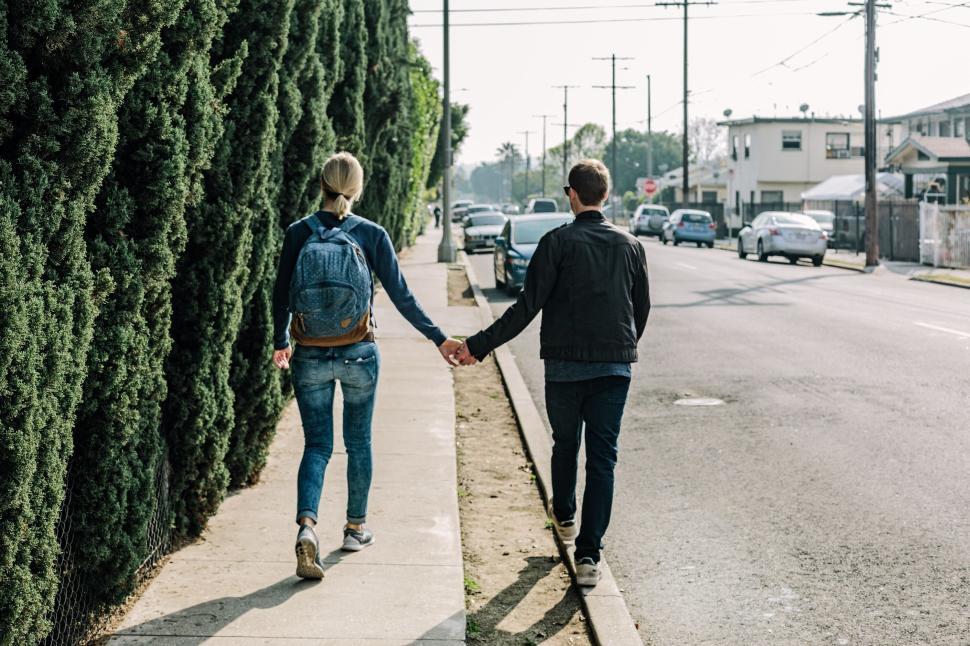Free Image of Couple walking hand-in-hand on sidewalk 