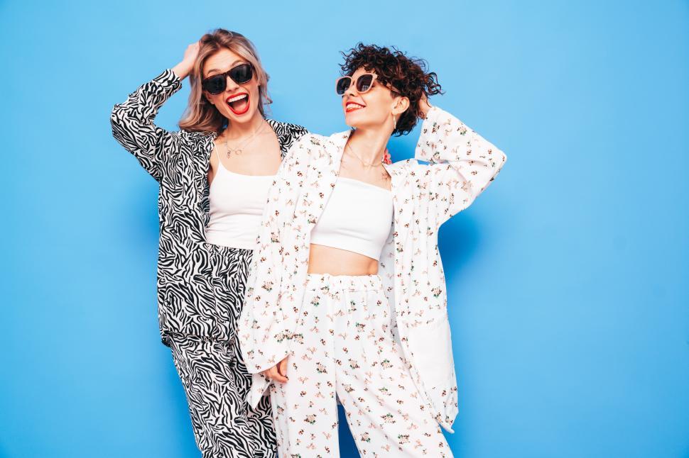 Free Image of Women smiling with sunglasses and stylish outfits. 