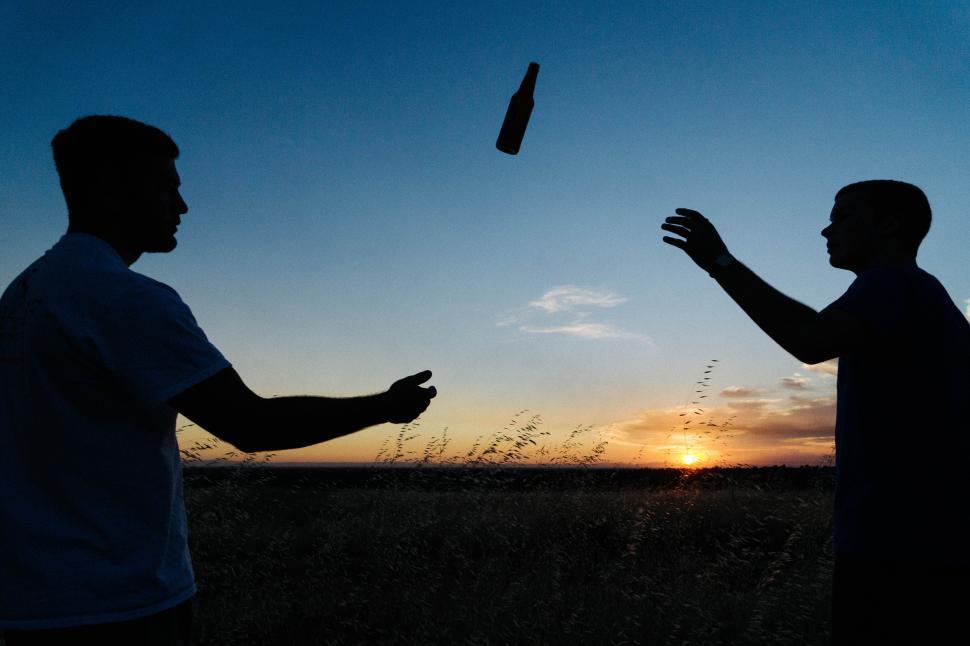 Free Image of Silhouettes tossing a bottle at sunset in a field. 