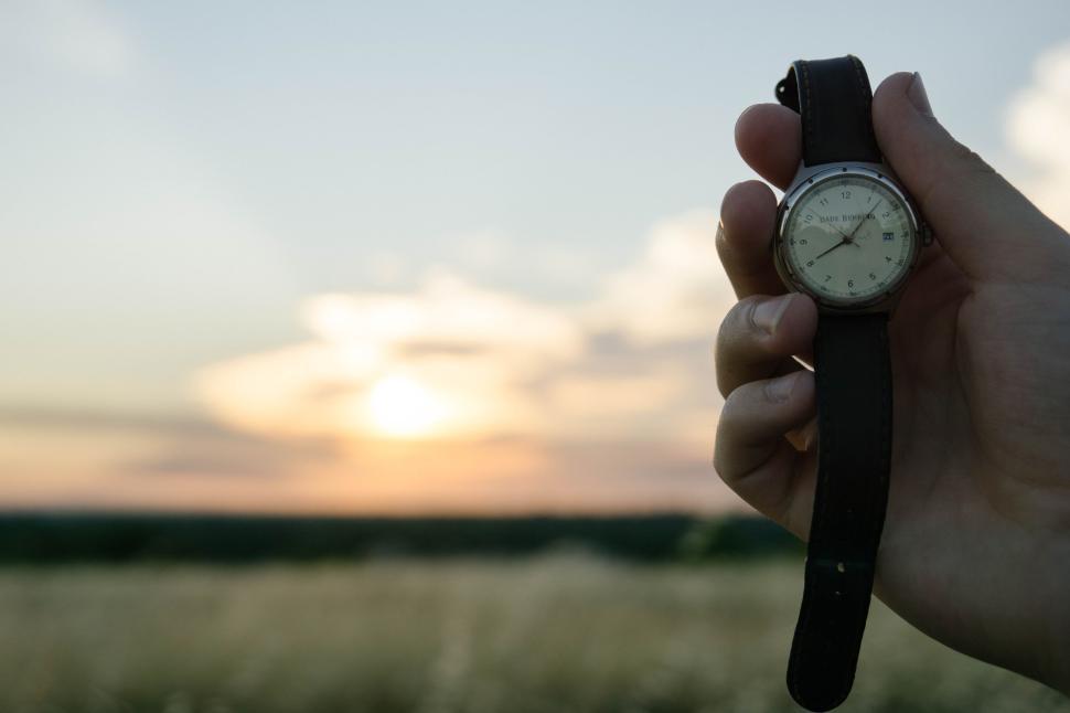 Free Image of Hand holding wristwatch with sunset in the background 