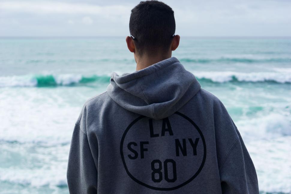 Free Image of Person standing by the ocean wearing a hooded sweatshirt 