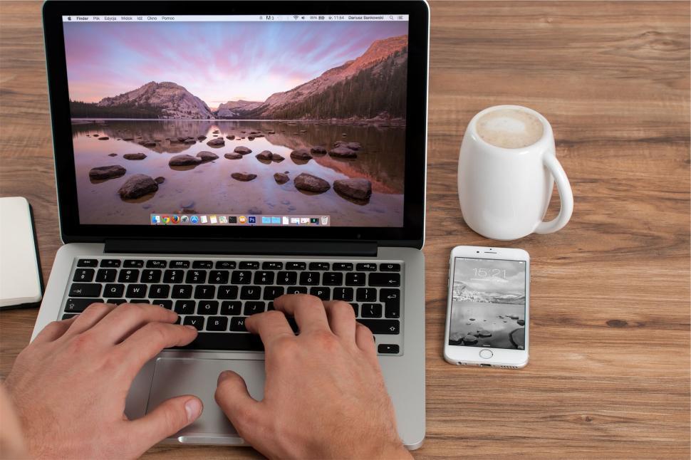 Free Image of Person typing on a laptop next to a smartphone and coffee 