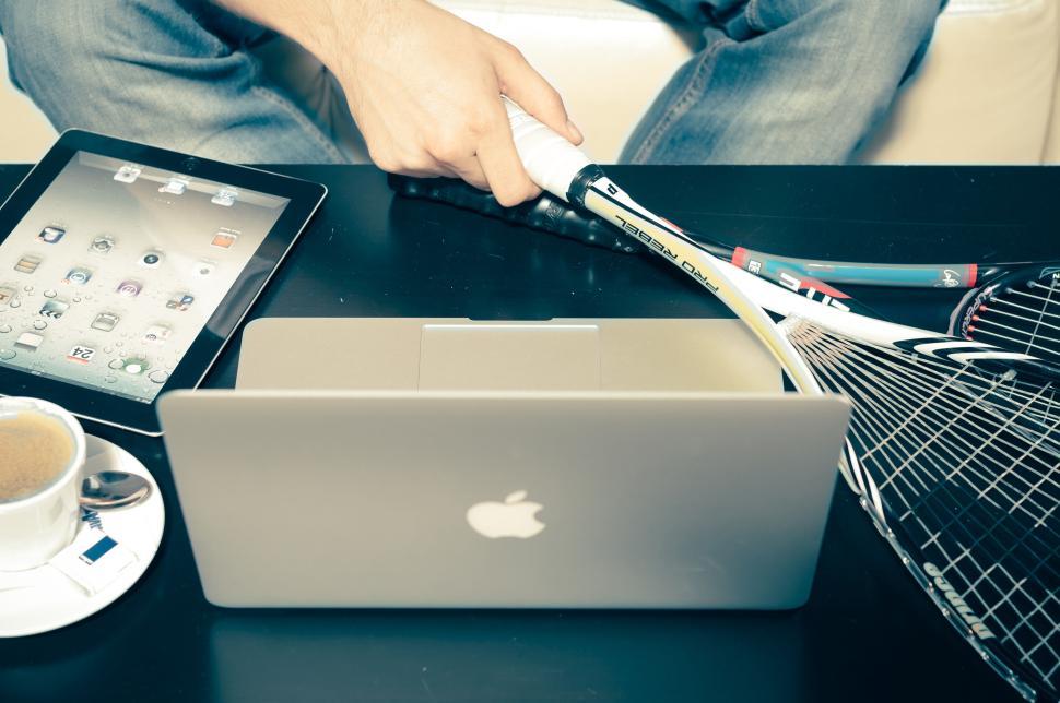 Free Image of Person holding a squash racket near a laptop setup 
