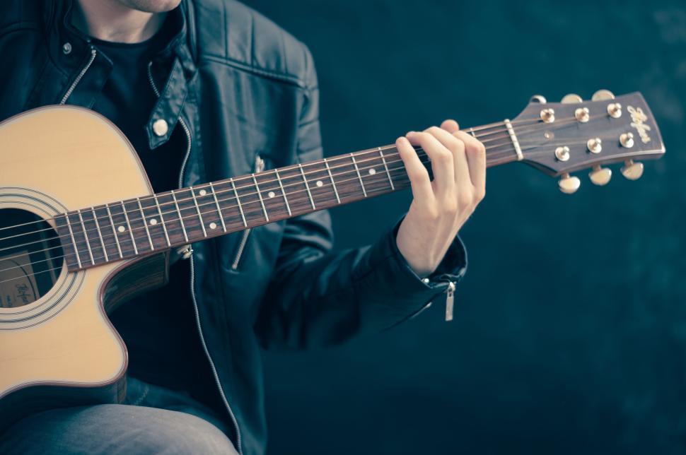 Free Image of Person in a leather jacket playing an acoustic guitar. 
