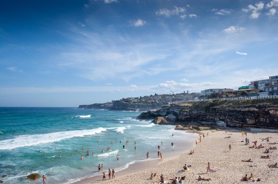 Free Image of Crowded beach with clear blue water and rocky landscape 