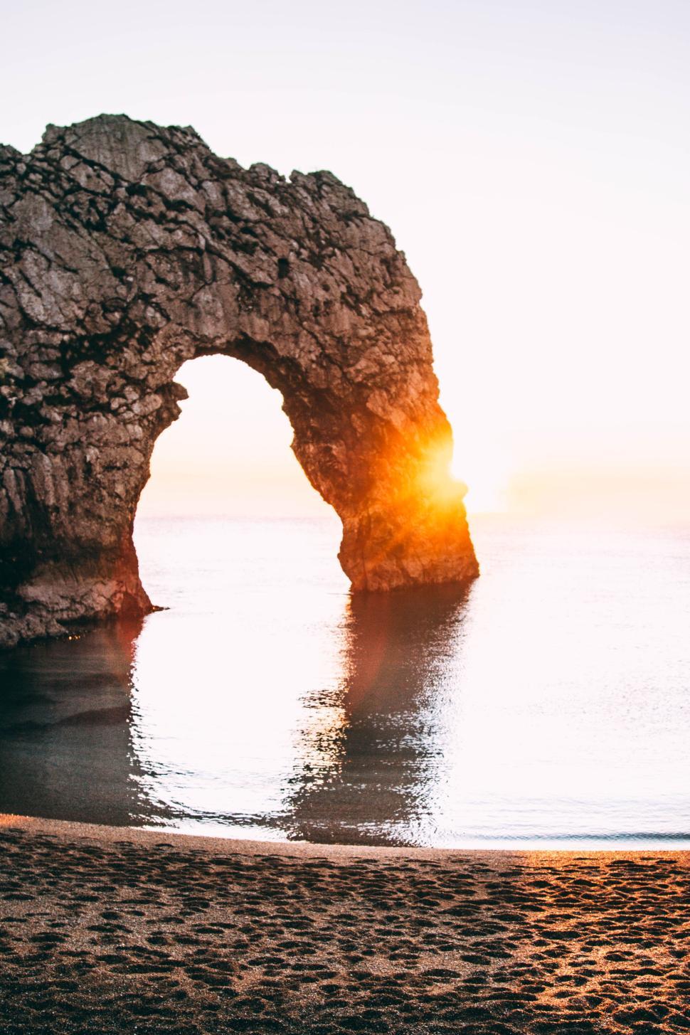 Free Image of Sunrise through natural stone arch at coastal beach site. 