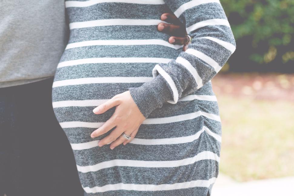 Free Image of Person embracing pregnant woman in striped dress outdoors 